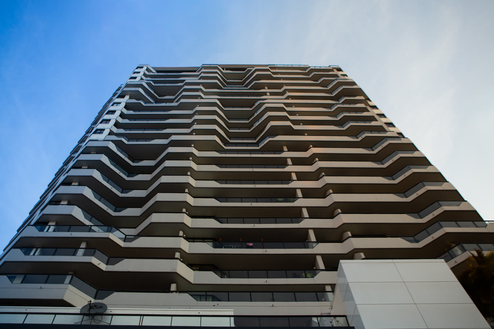 Balconied residential tower in Sydney shot upward against a deep blue sky