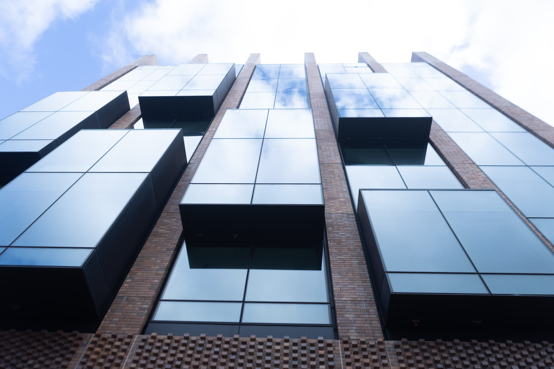 Glass and brick apartment facade in Sydney photographed from street level, sky reflected in the windows